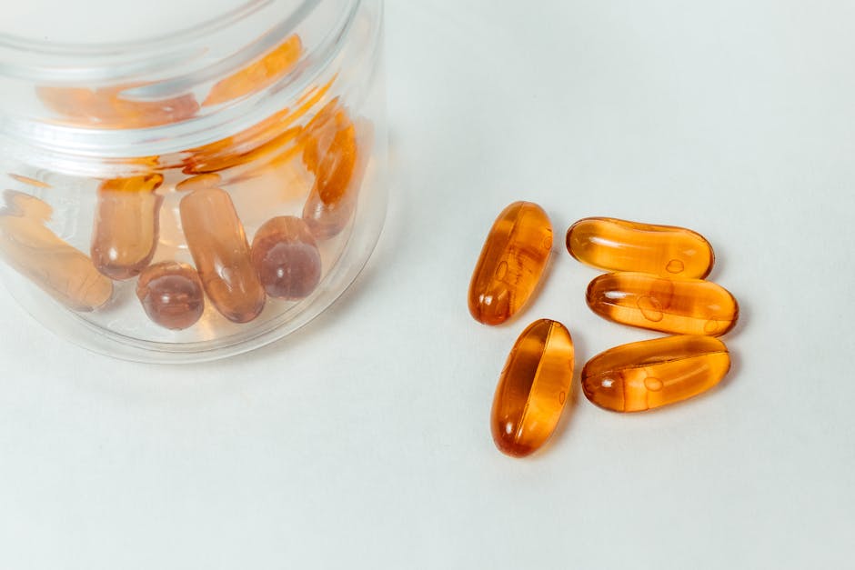 glass container with amber capsules spilling out on a white